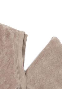 Tissu polaire beige avec une texture lisse, présentant des coutures visibles et une fermeture éclair, légèrement replié sur les bords.