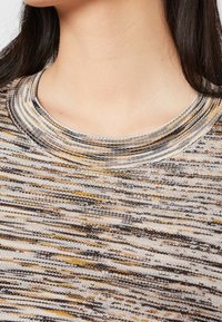 Stickad tröja med rund halsringning, som har ett flerfärgat mönster i beige, brunt och guld, med en strukturerad tygkvalitet.