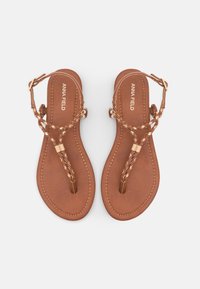 Sandales en cuir marron avec des brides tressées et des accents dorés. Semelle plate avec un design à lanière. Nom de la marque "ANNA FIELD" embossé sur la semelle intérieure.