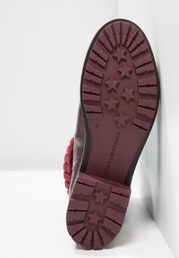 Bota burdeos con suela de goma texturizada que presenta patrones de estrellas; parte superior de cuero, punta redonda y un cuello de punto suave. Talla 37.