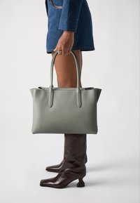 Siva usnjena torba z dvema zgornjima ročajema, pravokotne oblike, gladke teksture in minimalističnega dizajna, postavljena na svetlo ozadje.