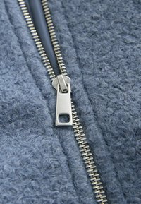 Material fleece gri cu o suprafață texturată, prevăzut cu un fermoar metalic argintiu pe centru pentru închidere.