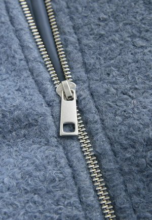 Grauer Fleece-Stoff mit strukturierter Oberfläche, ausgestattet mit einem silbernen Metallreißverschluss entlang der Mitte zum Schließen.