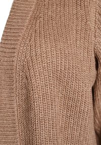 Maglione lavorato a maglia di una morbida tonalità marrone, con un design testurizzato a costine. Il tessuto appare caldo e accogliente, con motivi di cucitura visibili.