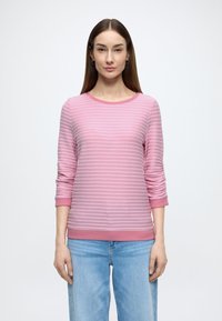 Roze gestreepte gebreide trui met lange mouwen, ronde halslijn, gestructureerd patroon en een effen gekleurde zoom. Draagt lichtblauwe jeans.