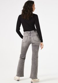 Graue, ausgestellte Jeans mit hoher Taille, fünf Taschen und einer dezenten, ausgebleichten Textur. Kombiniert mit einem enganliegenden schwarzen Langarmoberteil und Sneakers.