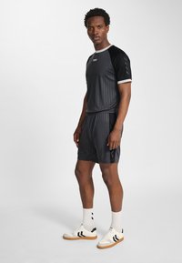 Svart sportskjorta med kritstrecksrand, matchande shorts och vita accenter. Bärs med vita sneakers med svart och gummisula.