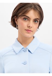 Lichtblauw overhemd met kraag, voorzien van twee knoopsluitingen en een gladde stoftextuur. Heeft een eenvoudig, klassiek ontwerp en een nette halslijn.