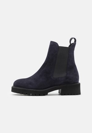 Navyblå ruskind ankle støvle med sort elastisk sidepanel, trækflap ved hælen og chunky sort gummisål med lav blokhæl.