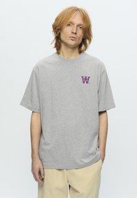 Grå bomulds T-shirt med korte ærmer, med et lilla "W" logo på venstre bryst. Løs pasform med rund hals.