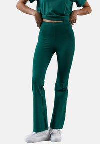 Rozszerzane zielone legginsy wykonane z elastycznej tkaniny, w połączeniu z dopasowanym krótkim topem. Posiadają gładką fakturę i brak widocznych wzorów.