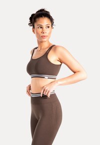 Top deportivo marrón y leggings de cintura alta a juego, con una banda de rayas blancas en contraste. Textura suave, diseño ajustado.