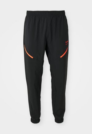 Pantalons de sport noirs avec taille élastique et poignets, dotés de poches zippées rouges en biais et d'un petit texte rouge de marque sur la cuisse droite.