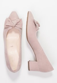 Chaussures à talons en suède rose avec un bout pointu et un grand nœud décoratif. Le talon est en forme de bloc et mesure environ deux pouces.