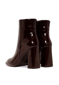 Bottines en cuir verni marron avec un design épuré, présentant une finition lisse, des talons blocs hauts et sans attaches ni embellissements visibles.