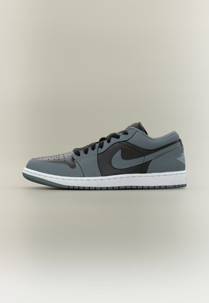 Alacsony szárú fekete és szürke Nike Air Jordan sportcipő fehér talppal, fekete fűzővel és perforált orr résszel, oldalnézetben.