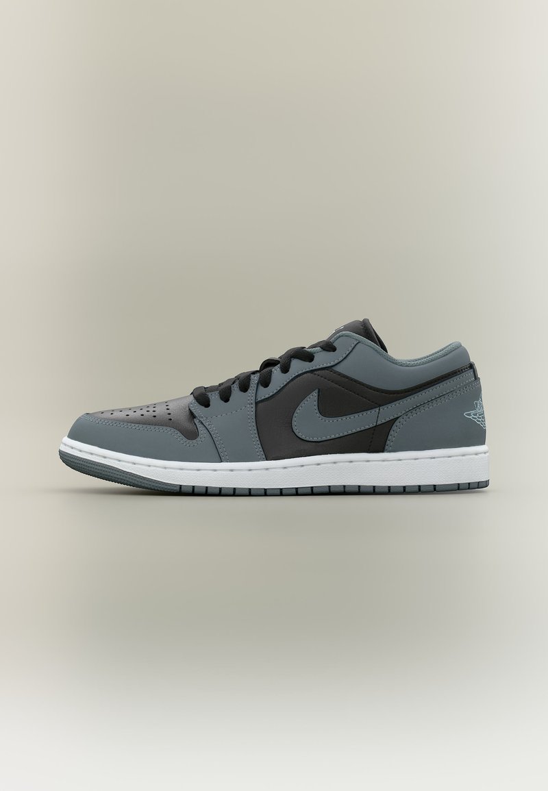 Χαμηλό μαύρο και γκρι αθλητικό παπούτσι Nike Air Jordan με λευκή σόλα, μαύρα κορδόνια και διάτρητη μύτη, εμφανιζόμενο στο προφίλ.