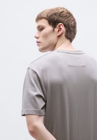 Szürke, rövid ujjú póló puha anyagból. Tiszta nyakkivágással, felhajtott ujjakkal és a hátulján kis varrás részlettel.