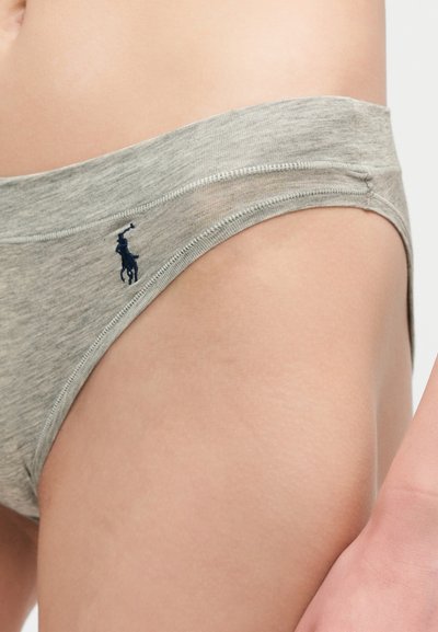 Κοντινή λήψη ενός ατόμου που φοράει ανοιχτό γκρι βαμβακερά εσώρουχα με ένα μικρό σκούρο κεντητό λογότυπο στο αριστερό ισχίο.