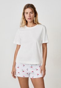 Biała bawełniana koszulka z krótkim rękawem, w połączeniu z białymi szortami z czerwonym wzorem wiśni i falbaniastym dołem.