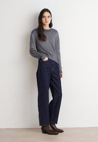 Chemise grise à manches longues, jean large bleu foncé et bottines à talons marron. Design simple avec une coupe décontractée et des détails minimalistes.