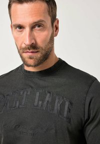 Sudadera negra con estampado texturizado "SALT LAKE" en el frente, cuello redondo acanalado y acabado en tela suave. Se aprecian detalles de costura.