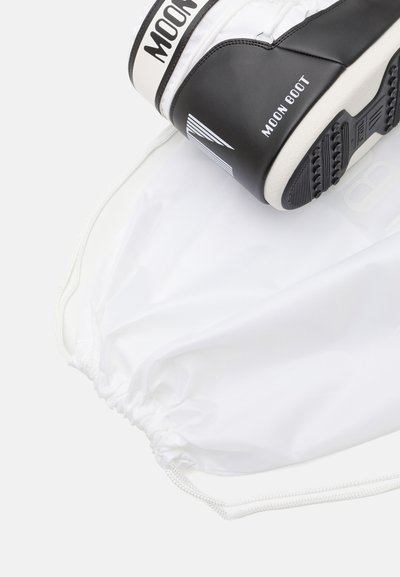 Zwart-witte Moon Boot met een glanzende afwerking, vergezeld van een witte trekkoordtas. Heeft een gestructureerde zool en logo-accenten.