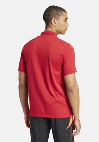 Rode polo shirt van gestructureerde stof, met korte mouwen en een oranje accent op de schouder, ontworpen voor een sportieve pasvorm.