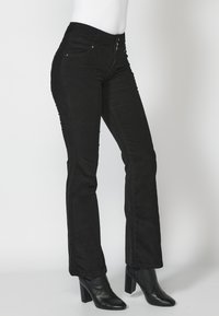 Jeans de pana negros con cintura alta, con cierre de botones, sutiles bolsillos frontales y diseño de pierna recta. Combinados con botas de tobillo negras.