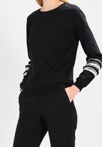 Svart långärmad sweatshirt med rund halsringning, med randiga texturerade detaljer på ärmarna och en slim-fit design.