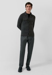 Szary wełniany kardigan z dwoma kieszeniami na piersi, zapinany na guziki z prążkowanym dołem, w połączeniu z szarymi, kratkowymi spodniami i czarnymi butami.