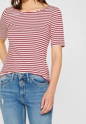 Kvinde iført en rød og hvid t-shirt med horisontale striber og korte ærmer, kombineret med højtaljede blå jeans med dobbelt knaplukning.