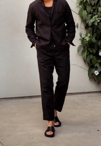 Czarna, lekka, długosłatowa koszula z guzikami, w zestawieniu z pasującymi spodniami i czarnymi sandałami. Gładka struktura, casualowy fason.