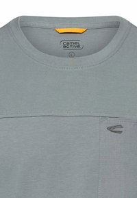 Lys grå t-shirt med rund hals, med en lille brystlomme, der har Camel Active-logoet og en størrelseetiket "L" inde i kraven.
