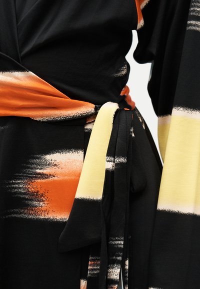 Μαύρο ύφασμα με αφηρημένα σχέδια με πινελιές σε πορτοκαλί, κρεμ και λευκό, δεμένο με κόμπο στη μέση.