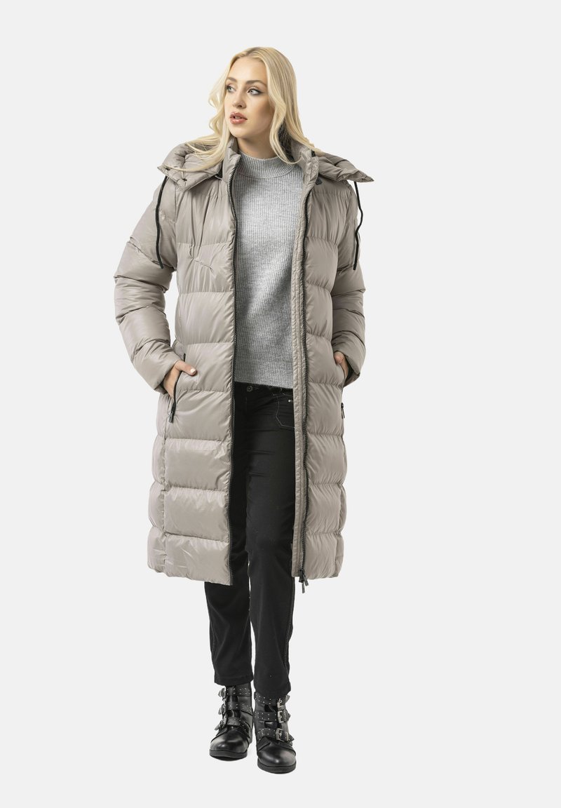 Lange, gevoerde jas in lichtgrijs met een capuchon, voorzien van doorgestikte secties en zwarte accenten, gecombineerd met een grijze trui en zwarte broek.