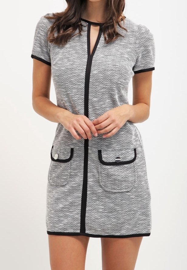 Šedé šaty v herringbonovém vzoru s krátkými rukávy, černými lemy, výstřihem ve tvaru klíčové dírky a dvěma předními kapsami s kovovými prvky ve stříbrné barvě.