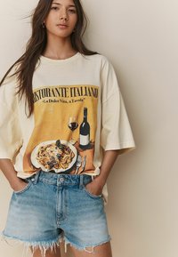 Ontspannen crème t-shirt met een grafische afbeelding van een Italiaans restaurant met pasta en wijn. Gecombineerd met lichte denim shorts met een rafelige zoom en zakken.