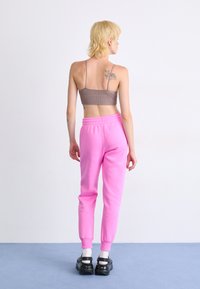 Rosa joggebukser med elastisk liv, grå ribbet bralette, og svart fottøy. Kort hår og synlige tatoveringer på ryggen.