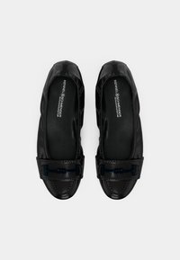 Paire de mocassins pour femmes en cuir noir avec boucles décoratives noires, vue de dessus sur fond blanc.