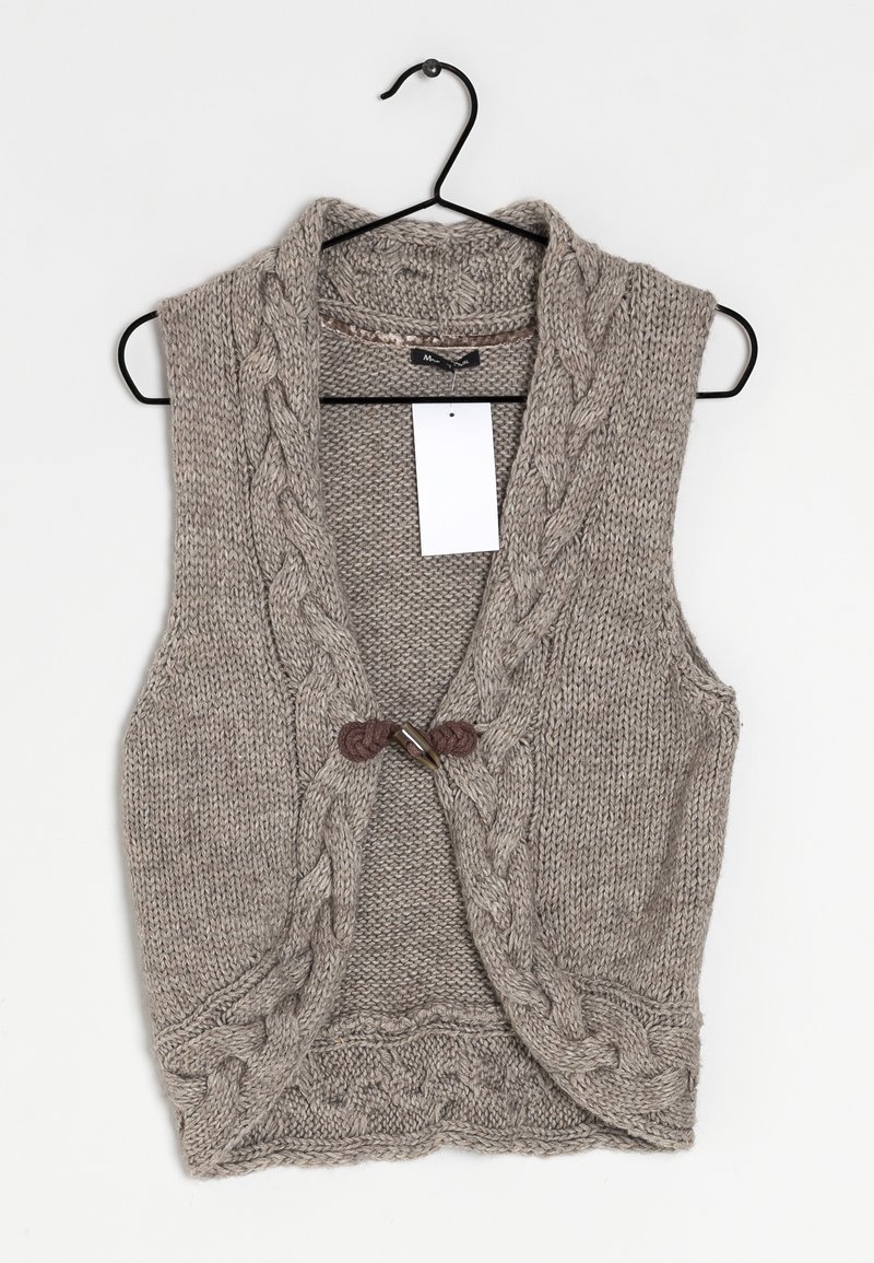Gilet sans manches beige tricoté avec des motifs tressés, fermeture à bascule en bois, suspendu à un cintre noir avec une étiquette blanche.