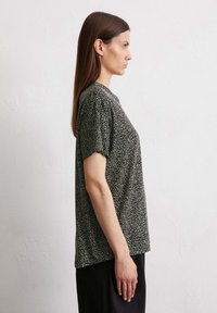 Zwart-wit korte mouwen t-shirt met een stippenpatroon, ronde hals en een relaxte pasvorm, gedragen met donkere broek.
