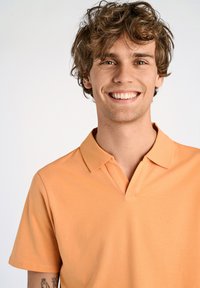 Polo shirt arancione a maniche corte con colletto, caratterizzato da una texture in cotone liscia e una vestibilità rilassata. Nessun motivo o accento visibile.