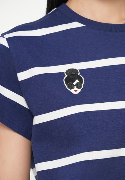 Ναυτικό μπλουζάκι με ριγέ σχέδιο, λευκές οριζόντιες ρίγες και μικρή κεντημένη απεικόνιση μιας γυναίκας με γυαλιά ηλίου και κόκκινα χείλη στο στήθος.