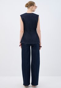 Top de mezclilla sin mangas con un corsé ajustado y dobladillo acampanado, combinado con vaqueros de pierna ancha de cintura alta en azul oscuro. Textura suave, líneas limpias.