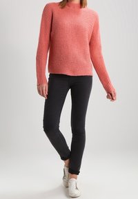 Pull rose en maille texturée à manches longues, associé à un jean noir slim et des baskets blanches. Tenue simple et décontractée.