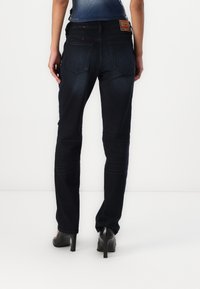 Mörk denimjeans med rak bendesign, som har en blekt textur, röda sömnadsdetaljer och en läderlapp på midjebandet.