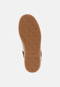 Suola di scarpa in gomma color sabbia con un motivo testurizzato caratterizzato da forme a diamante e il nome del marchio "GUESS" in evidenza al centro.