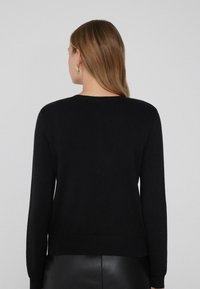 Schwarzer Strickpullover mit langen Ärmeln, rundem Ausschnitt und geripptem Saum. Glatte Textur und taillierte Passform, kombiniert mit einem Lederrock.