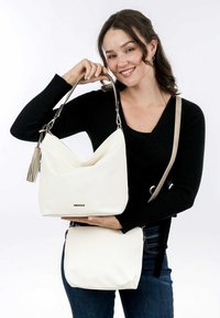 White faux leather handbag with a slouchy design, metal hardware, and a detachable strap, held alongside a smaller matching bag.